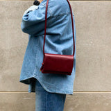 8 of 8:Person wearing a red crossbody bag and blue denim outfit against a beige wall.