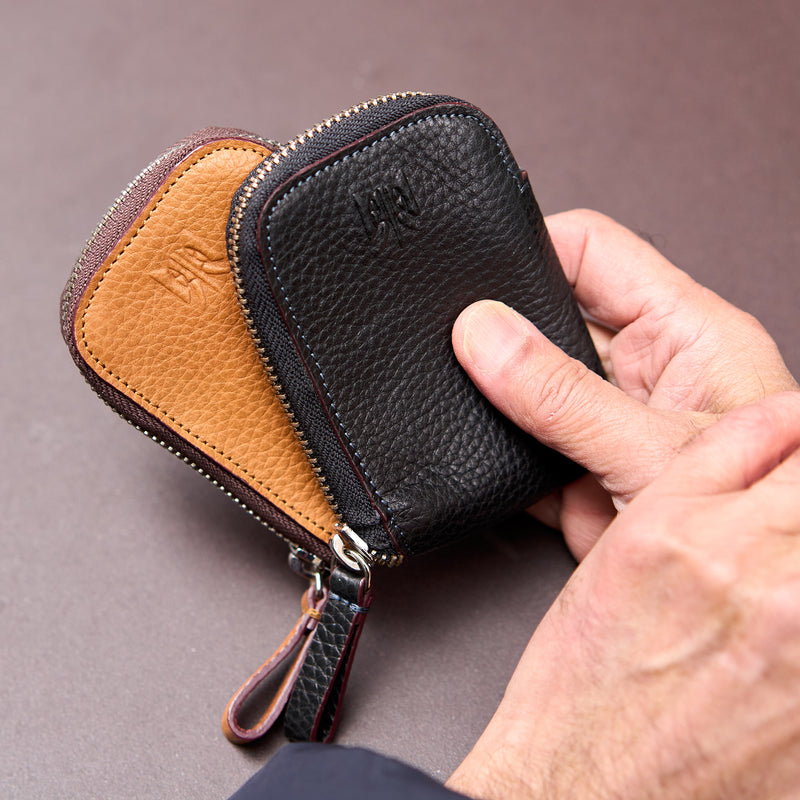 Hand holding a black and tan leather zippered wallet on a gray background