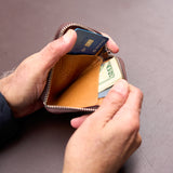 8 of 9:Person opening a leather wallet with money and a card on a brown background