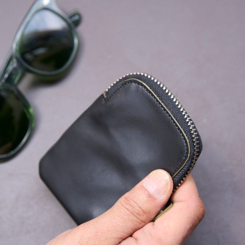 Black leather wallet held by a hand with sunglasses in the background on a gray surface