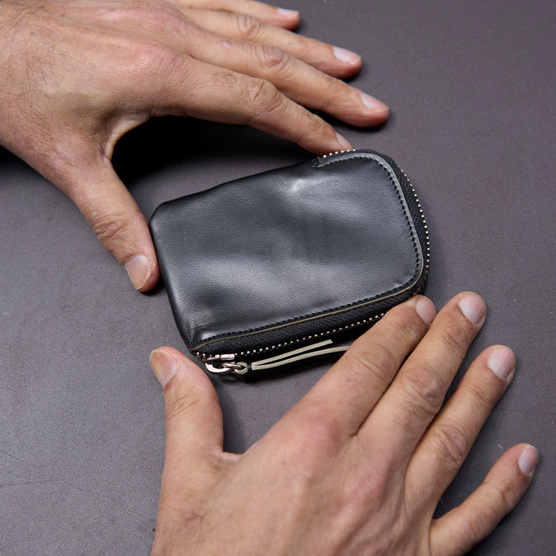 Black leather wallet being held by a person's hands on a gray surface