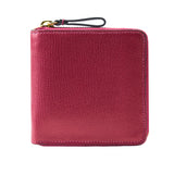 9 of 39:A small pebbled leather zip-around wallet in a rich magenta pink color, featuring a black wristlet loop with a gold-tone metal ring on the top left, set against a plain white background.
