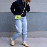 25 of 27:A person walking outdoors wearing a black jacket, light blue jeans, tan sneakers, and carrying a bright yellow-green crossbody bag with a matching strap.