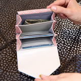 3 of 22:Person opening a pink polka dot wallet to reveal cards and money on a patterned surface.