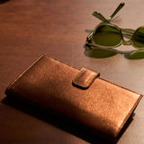 7 of 15:A pair of green-tinted sunglasses resting on a metallic bronze surface next to a matching bronze leather case.