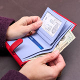 3 of 8:Person holding a red and blue wallet with money and an ID card on a dark surface