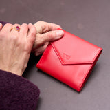 2 of 8:Red wallet with 'TUSK' branding held by a person's hand on a gray background