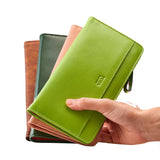 45 of 55:A hand holding a stack of textured leather zip-around wallets in lime green, brown, dark green, and blush pink against a white background.