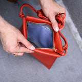 3 of 5:Orange leather handbag with a clear compartment held by hands on a gray surface