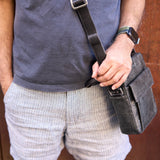 6 of 10:Person holding a black shoulder bag against a wooden background