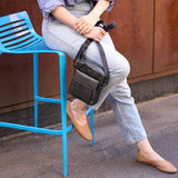 7 of 10:Person sitting on a blue stool wearing light blue jeans and brown shoes, with a wooden wall in the background.