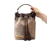 3 of 7:Leopard print bucket bag with brown drawstring and tassel held by a hand on a white background