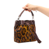 11 of 29:Leopard print handbag with brown leather accents held by a hand on a white background