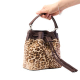 4 of 29:Leopard print handbag with brown handle and strap held by a hand on a white background