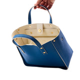 5 of 18:Blue handbag with beige interior held by a hand on a white background
