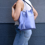 4 of 23:Person holding a light blue bucket bag with tassels against a gray wall