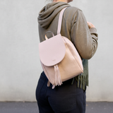 2 of 5:Person wearing a pink and beige backpack with a plain background