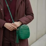 3 of 16:Person holding a green round purse with a textured surface and tassel detail.