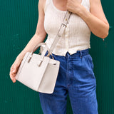 3 of 11:Person holding a white handbag against a green background