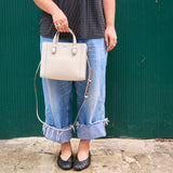 2 of 11:Person holding a beige handbag against a green wall