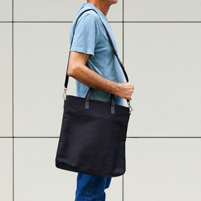 Person carrying a black shoulder bag against a light gray wall