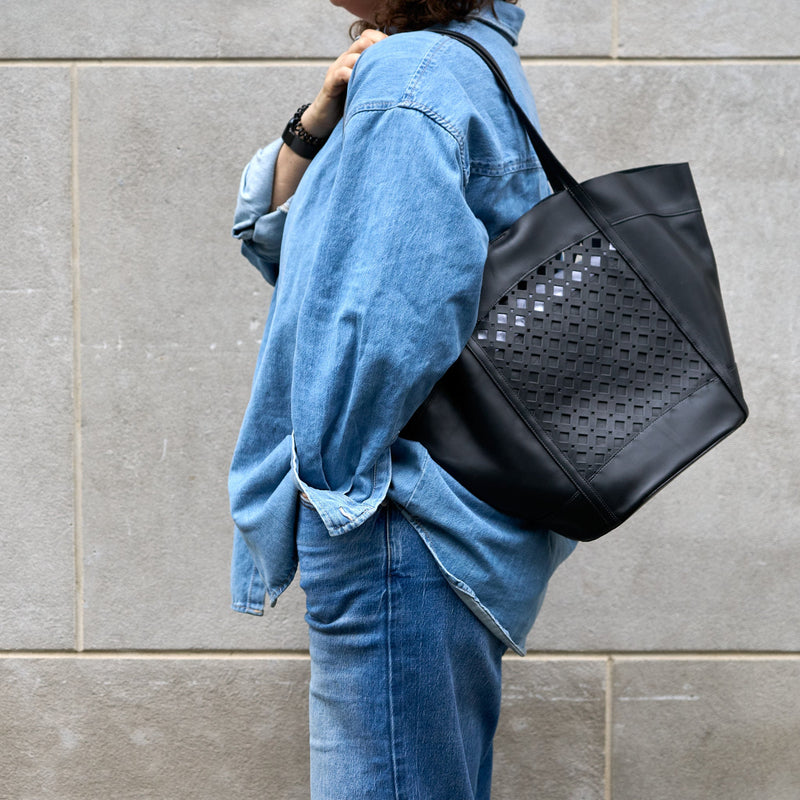 Person wearing a black perforated handbag against a gray wall