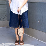 4 of 15:Person wearing blue shorts and a white top, holding a zebra print handbag against a gray wall.