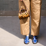 2 of 43:A person wearing tan wide-leg pants and blue sandals holds a small leopard-print handbag with brown leather trim against a gray brick wall - CAMEL/BLACK
