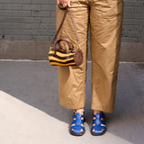 8 of 43:A person wearing tan cropped pants and blue sandals holds a small striped handbag with brown leather trim against a gray brick wall background - ORANGE/BLACK