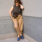 17 of 43:A woman leans against a gray concrete wall wearing a dark gray sleeveless top, tan cargo pants, blue sandals, and a small brown crossbody bag.