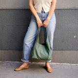 4 of 15:Person holding a green bag against a gray wall