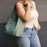 2 of 15:Person holding a light green handbag against a gray wall