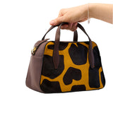 4 of 64:Handbag with cow print pattern held by a hand on a white background