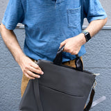 3 of 20:Person holding a black bag against a gray wall