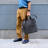 2 of 20:Person holding a black leather bag against a gray wall