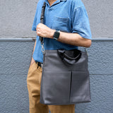 4 of 20:Person holding a dark gray shoulder bag against a gray wall