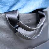 5 of 20:Close-up of a gray handbag with a black ribbon handle.