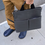 6 of 20:Person holding a dark gray leather briefcase on a sidewalk.