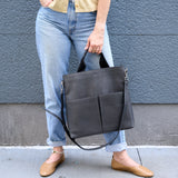 12 of 20:Woman holding a grey leather tote against a gray wall.