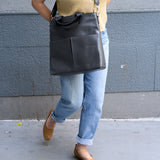 13 of 20:Person wearing a grey shoulder bag with a gray wall background