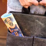 4 of 16:Person holding a leather bag with a New York-themed product peeking out.