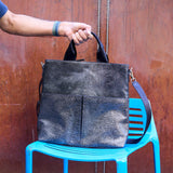 11 of 16:Person holding a black leather bag over a blue chair against a wooden background