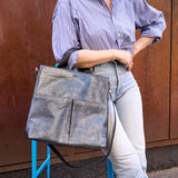 13 of 16:Person holding a gray leather bag on a blue stool against a rust-colored wall.