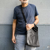 3 of 16:Man holding a gray bag against a gray wall