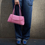 2 of 20:A person wearing blue pinstripe jeans and blue sandals holds a pink leather shoulder bag against a textured gray concrete wall - BLUSH