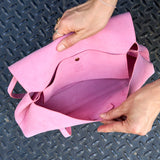 9 of 20:A pink suede tote bag being held open by two hands over a dark textured diamond-plate metal surface -  BLUSH